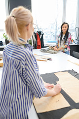 Young female designer choosing fabric and talking to dressmaker in atelier