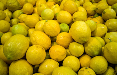 Piles of fresh different in shape lemons on a market