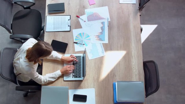 top view business worker sitting at the workplace typing on computer in modern office. on the desk different documents sheets of information in the form of a table, graph, or diagram.