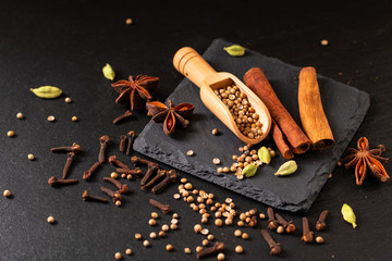 Exotic herbal Food concept Mix of the organic Spices cinnamon stick, cardamom pods, star anise and coriander seeds on a black slate stone plate with copy
