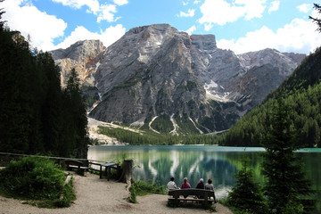 Four tourists sit on a bench near the Lake Braies (Lago di Braies) and admire the amazing view of Dolomites Alps