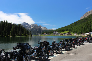 Several motorbikes parked in a row along the Misurina Lake shore with view of Dolomites Alps mountains