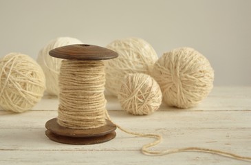 Fototapeta na wymiar Spool of yarn thread and balls on white wooden background close-up.