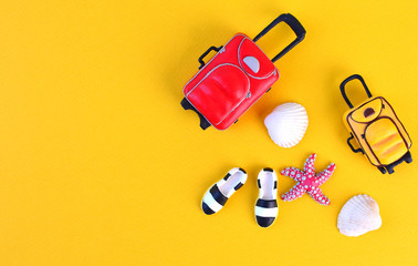 Miniature traveler accesories on yellow background with bags, moccasins, seashells and starfish. Summer travel background.