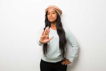 Young afro american woman on white wall making stop gesture with her hand denying a situation that thinks wrong