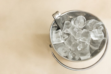 A silver bucket made from aluminum full filled with ice cube is placed on the table at the pub, ice were made for make water, whisky, vodka or alcohol drinking cold