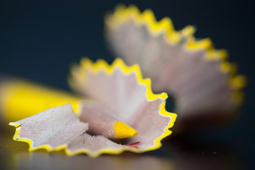 Yellow pencil and shavings on black background. Closeup
