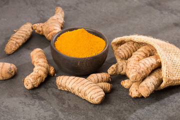 Turmeric powder and fresh turmeric on wooden background