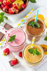 Strawberry, chocolate and apricot milkshake or smoothies on a white wooden background. Healthy juicy vitamin drink diet or vegan food concept.