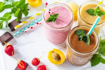 Strawberry, chocolate and apricot milkshake or smoothies on a white wooden background. Healthy juicy vitamin drink diet or vegan food concept. Copy space.