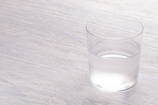 A close-up image of a wet steaming glass of water half full. On a white wooden table.