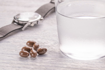 Misted glass of water and brown medical capsules on a white old wooden table. Wrist Watch