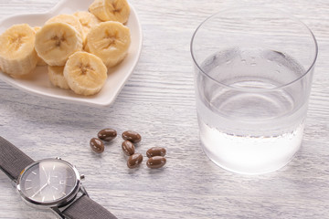 Sliced and whole bananas. On a white plate. On the old wooden table. Misted glass with clean water