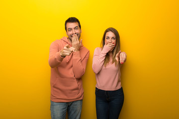 Group of two people on yellow background pointing with finger at someone and laughing