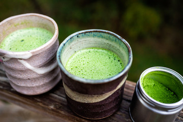 Wooden railing outside on backyard deck garden and two cups filled with Japanese vibrant green tea...