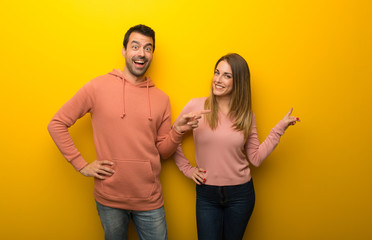 Group of two people on yellow background pointing finger to the side and presenting a product