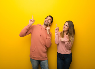 Group of two people on yellow background pointing with the index finger and looking up