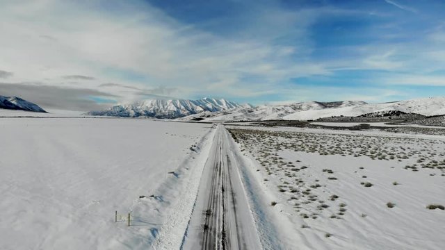 Aerial-Pull back over snowy road leading to vanishing point toward majestic snow-covered mountain under blue sky with wispy clouds