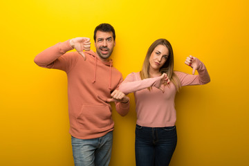 Group of two people on yellow background showing thumb down with both hands