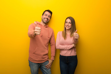 Group of two people on yellow background giving a thumbs up gesture because something good has...