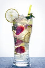 Freshly made refreshing mojito in a tall glass with strawberry, lime, fragrant mint leaves and ice on a light background