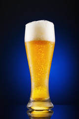 Full glass of freshly poured beer on a blue background