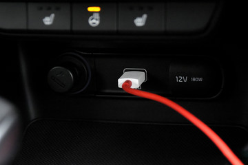 Black leather car control panel with blurred buttons and red usb cable for smartphone charging. Electronic dashboard of a car with red charger plug for cell phone with selective focus. 