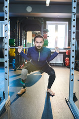 Portrait of young sportsman with artificial leg working out with barbell at gym