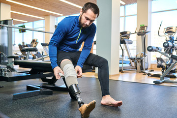 Handsome bearded athlete sitting and bandaging his leg before training in fitness club