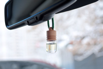 Car air perfume freshener inside the car with blurred winter background. Little glass bottle with wooden lid and yellow aromatic liquid automobile freshener on a green rope and car mirror 