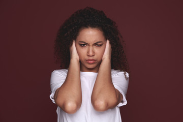 African woman covering ears with her hands, over a pink background