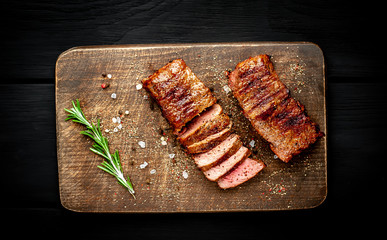 Beef steak on the cutting board with spices, wooden dark table