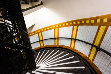 London, UK Covent Garden tube station underground spiral steps staircase down with nobody on stairs yellow colorful architecture - Powered by Adobe