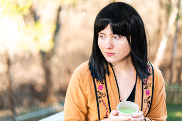 Woman holding tea cup on outside in backyard garden with girl and green matcha black hair and asian...