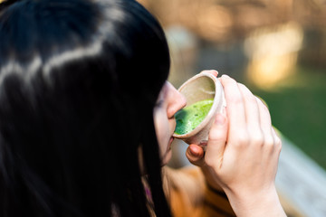 Woman holding tea cup face closeup drinking outside in backyard garden with girl and green matcha black hair