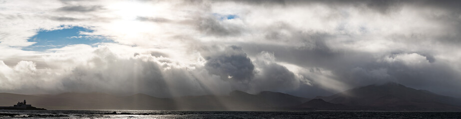 Naklejka na ściany i meble Sunlight breaking through storm clouds on the west coast of Ireland, dramatic panorama landscape 
