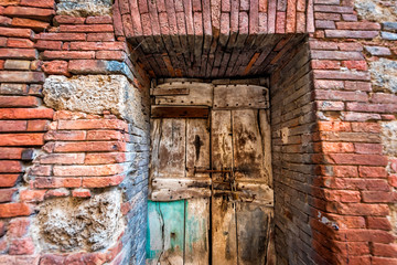 Chiusi, Italy street in small historic medieval town village in Umbria with closeup of colorful red orange stone brick wall and wooden ancient door
