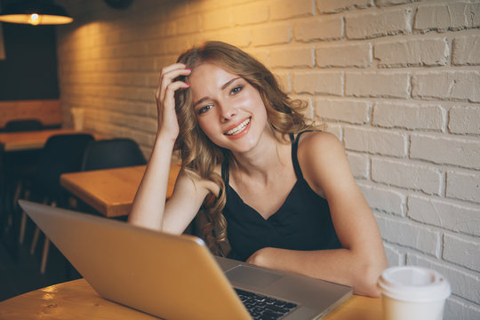 Photo of attractive yong girl with curly hair sitting in a coffee shop working by her laptop, femail freelance