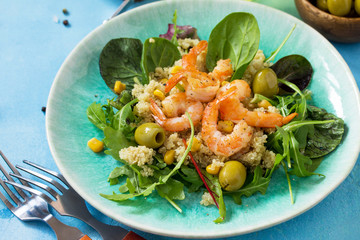 Diet menu, Vegan food. Healthy salad close-up with quinoa, arugula, Shrimps and olives on a blue stone table.