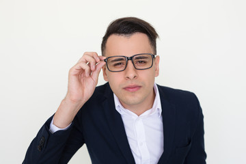 Fototapeta na wymiar Concerned guy in office clothes staring at camera through eyewear. Young Caucasian man in jacket touching glasses and posing. Sight or vision concept