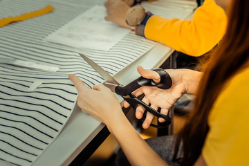 Top view of girl using scissors while cutting striped fabric