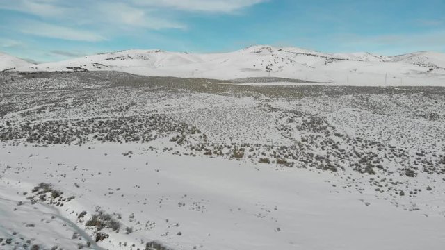 Aerial-Rising and flying over snowy field to snow-covered hills speckled with sagebrush