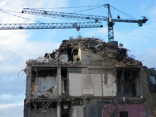 large cranes over a large concrete building being demolished with exposed walls during...