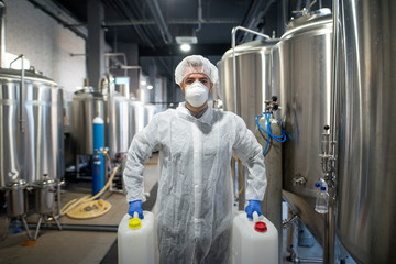 Industrial worker holding plastic cans with chemicals in production plant. Technologist wearing...