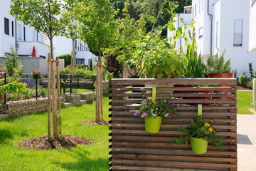 Moderner Gartenbau: Mit Holzwänden verkleidete Mülltonnen vor frisch gepflanzten Obstbäumen 