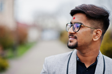Obraz premium Close up head of stylish indian man with bindi on forehead and glasses, wear on suit posed outdoor.