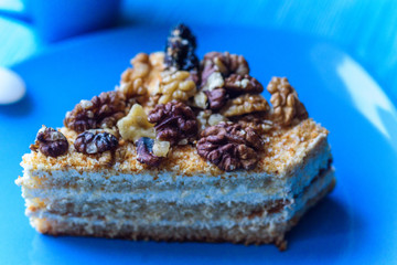 Walnut sponge cake slice photographed close-up on a turquoise plate, on wooden background.
