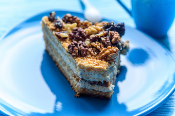 Walnut sponge cake slice photographed close-up on a turquoise plate, on wooden background.