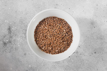 Flax seeds in a white bowl on a gray kitchen table. Organic health food