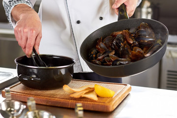 Chef transferring shell mussels from pan to saucepan. Just fried fresh seafood transferring using kitchen tongs.